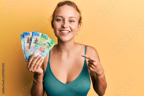 Beautiful caucasian woman holding swiss franc banknotes smiling happy pointing with hand and finger