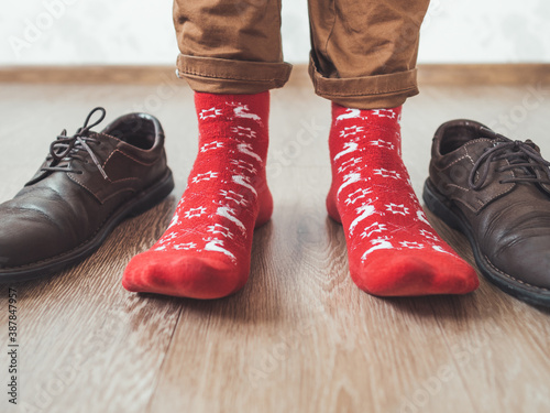 Young man in chinos trousers and bright red socks with reindeers on them is ready to wear sude shoes. Scandinavian pattern. Winter holiday spirit. Casual outfit for New Year and Christmas celebration. photo