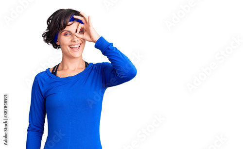 Beautiful young woman with short hair wearing training workout clothes doing ok gesture with hand smiling  eye looking through fingers with happy face.