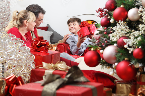 merry christmas, happy family at home, parents giving the gift to their child near the illuminanted and decorated tree, joyful and smiling sitting in the living room and comforted by the fireplace  photo