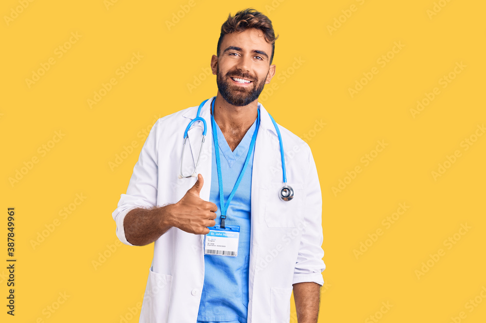 Young hispanic man wearing doctor uniform and stethoscope doing happy thumbs up gesture with hand. approving expression looking at the camera showing success. Young hispanic man wearing doctor uniform and stethoscope doing happy thumbs up gesture with hand. approving expression looking at the camera showing success.