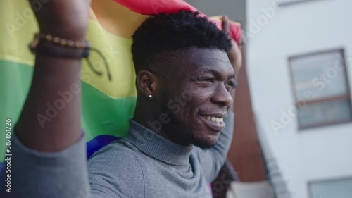 Young handsome homosexual black man holding rainbow flag on the balcony. High quality 4k footage
