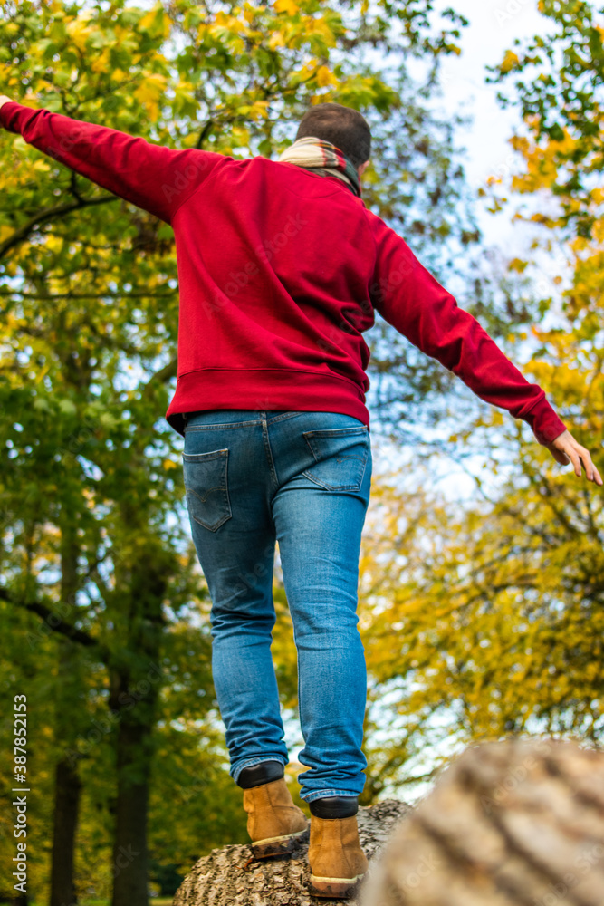 Photo of the legs on a young man wearing mountain boots and jeans walking in a tree trunk during an autumn day in the park