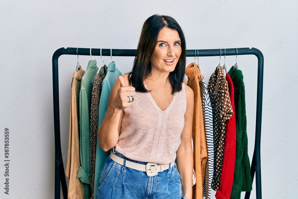 Middle age brunette woman working as professional personal shopper doing happy thumbs up gesture with hand. approving expression looking at the camera showing success. - obrazy, fototapety, plakaty 