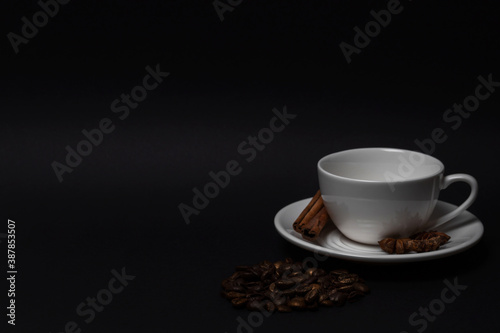 Empty white cup and saucer, coffee beans, cinnamon sticks, anise