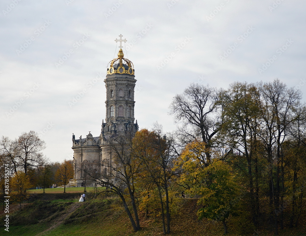An autumn Russian landscape in yellow and green, with bare trees, beautiful old cathedral and a newly-married couple