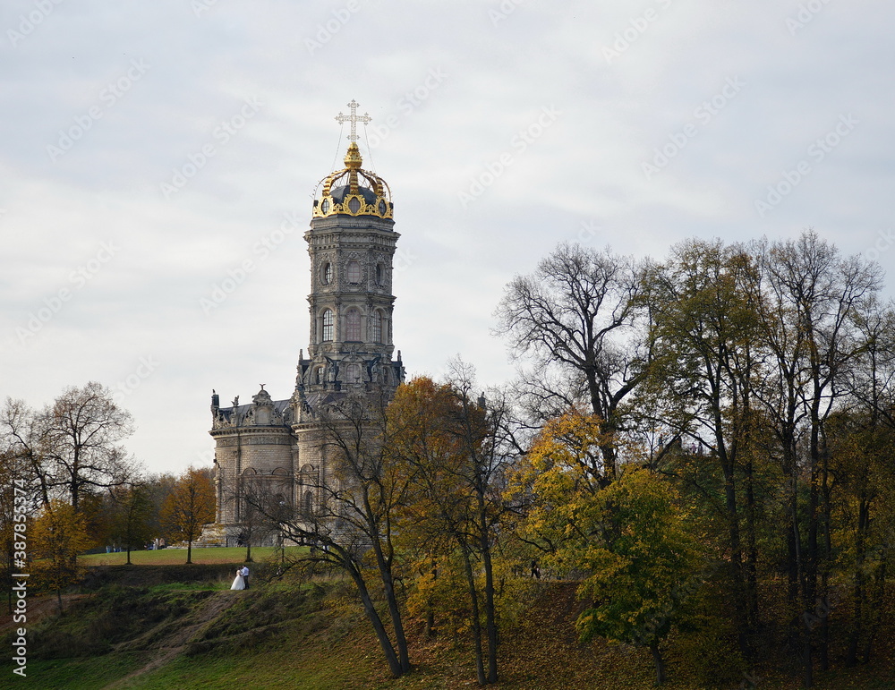 Obraz premium An autumn Russian landscape in yellow and green, with bare trees, beautiful old cathedral and a newly-married couple