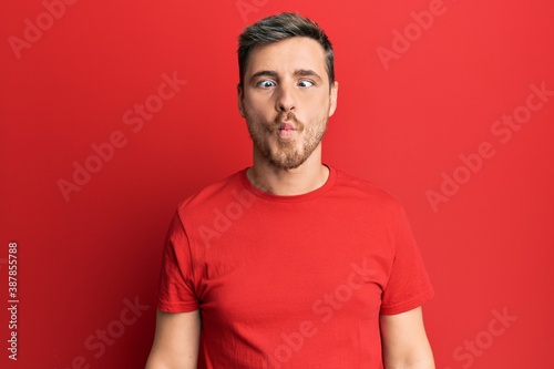 Handsome caucasian man wearing casual red tshirt making fish face with lips, crazy and comical gesture. funny expression.