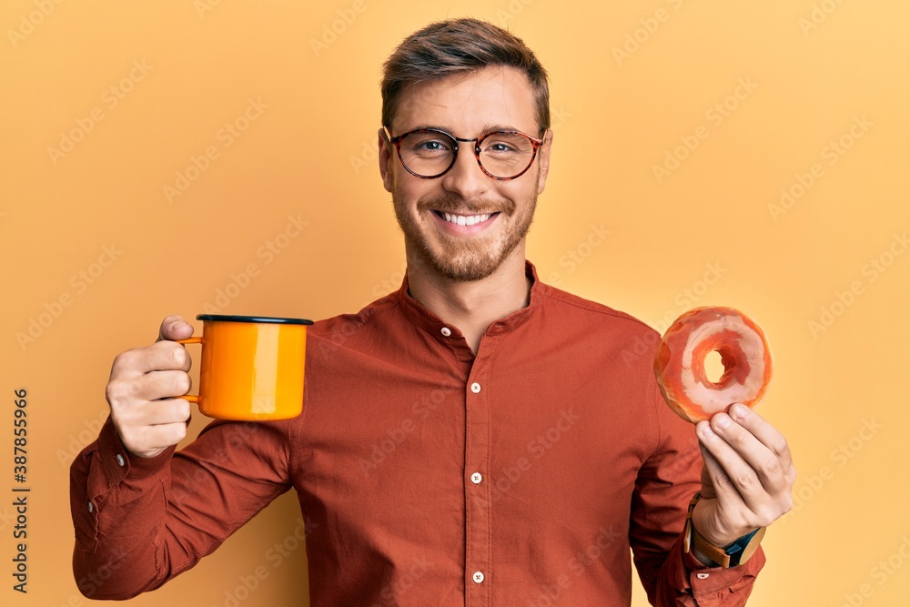 Fototapeta premium Handsome caucasian man eating doughnut and drinking coffee smiling with a happy and cool smile on face. showing teeth.
