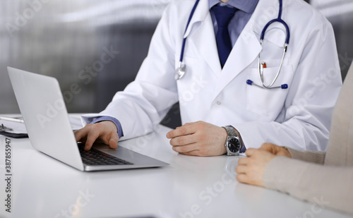 Unknown male doctor and patient woman discussing something while sitting in clinic and using laptop. Best medical service in hospital  medicine  pandemic stop