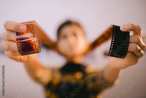 Happy young female holding filmstrip and smiling. Portrait of creative girl photographer in photo studio darkroom. Developing analog camera film