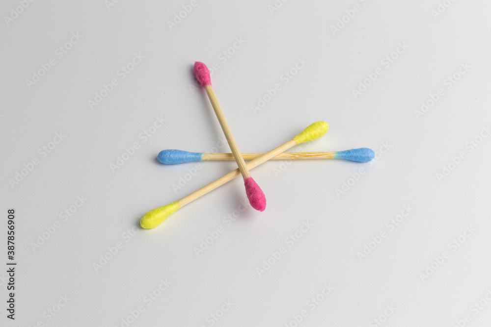 Pink, blue and yellow wooden cotton ear swabs or sticks on white background. Recycling and sustainability problem in everyday reasonable consumption. Colourful lifestyle, isolated, close-up. Pink, blue and yellow wooden cotton ear swabs or sticks on white background. Recycling and sustainability problem in everyday reasonable consumption. Colourful lifestyle, isolated, close-up.