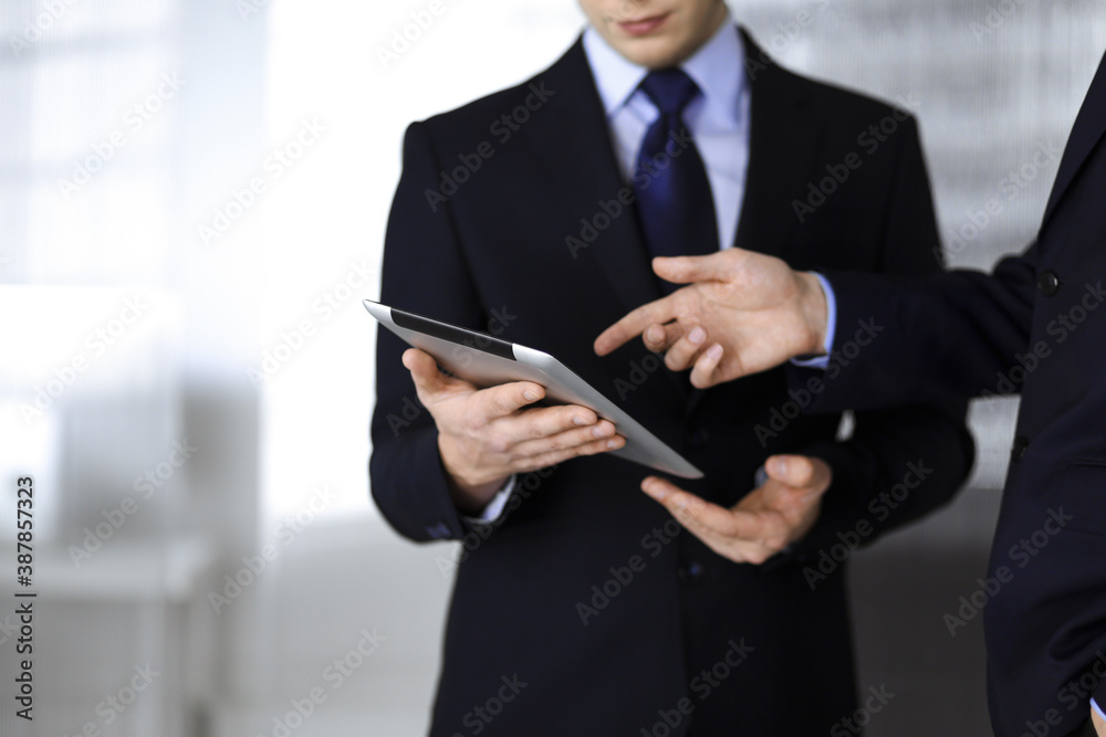 Business people use a tablet computer for discussion of their new project, standing in a modern office. Unknown businessman or male entrepreneur with a colleague at workplace. Teamwork and partnership Business people use a tablet computer for discussion of their new project, standing in a modern office. Unknown businessman or male entrepreneur with a colleague at workplace. Teamwork and partnership