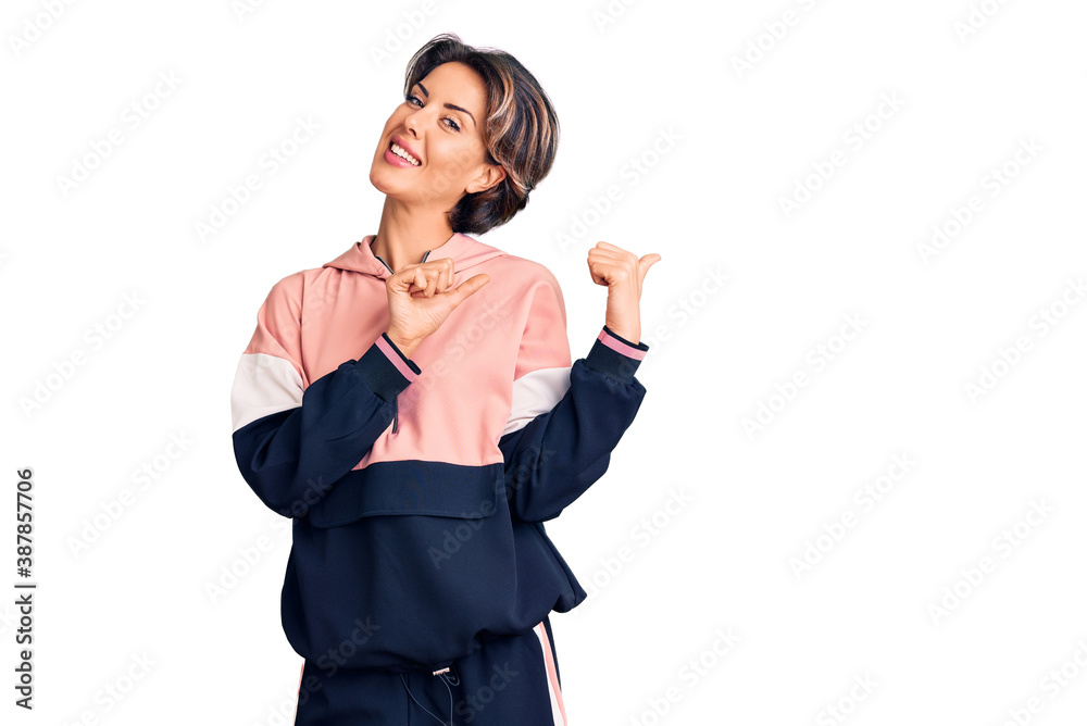 Young beautiful woman wearing sportswear pointing to the back behind with hand and thumbs up, smiling confident Young beautiful woman wearing sportswear pointing to the back behind with hand and thumbs up, smiling confident
