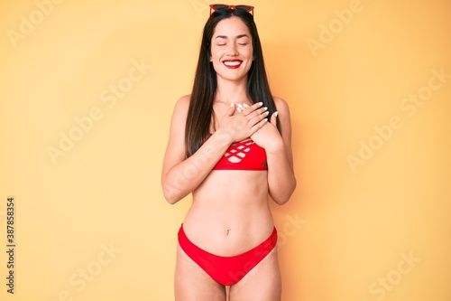 Young beautiful caucasian woman wearing bikini smiling with hands on chest with closed eyes and grateful gesture on face. health concept.