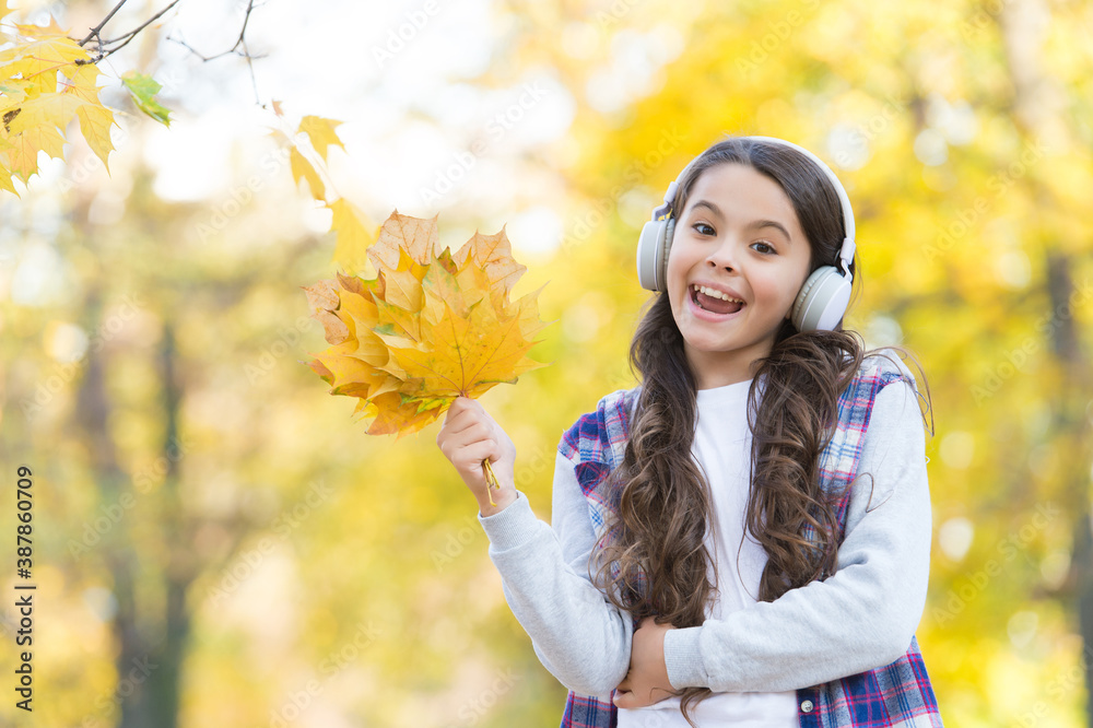 happy child in casual style spend time in autumn forest with maple leaves enjoying good weather while listening music in headphones, online education