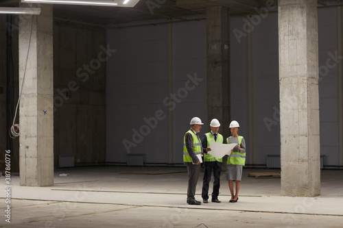 Wide angle portrait of business people wearing hardhats and holding plans while standing at construction site indoors  copy space