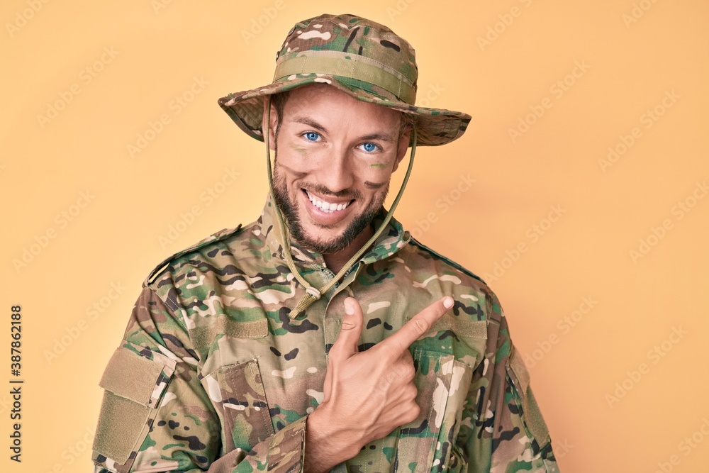 Young caucasian man wearing camouflage army uniform smiling cheerful pointing with hand and finger up to the side Young caucasian man wearing camouflage army uniform smiling cheerful pointing with hand and finger up to the side