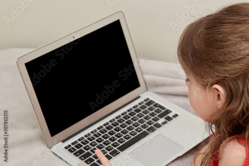 Girl look at the blurry black laptop screen. Online training. Learn at home lying on the bed.