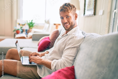 Handsome caucasian man smiling happy sitting on the sofa using computer laptop working from home