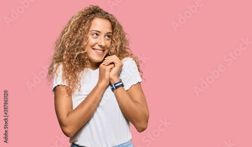 Beautiful caucasian teenager girl wearing casual white tshirt laughing nervous and excited with hands on chin looking to the side