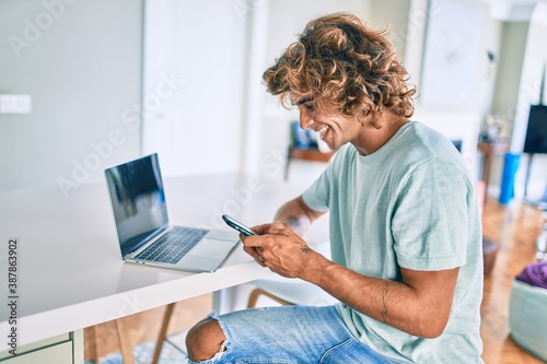 Young hispanic man smiling happy using smartphone sitting on the table at home