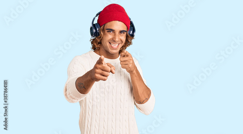 Young hispanic man listening to music using headphones pointing fingers to camera with happy and funny face. good energy and vibes.