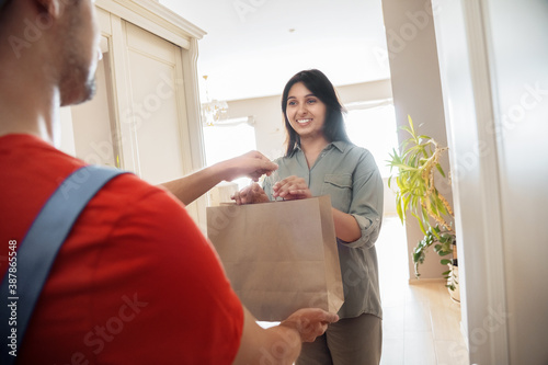 Indian woman customer taking delivery paper eco bag with grocery takeout food meal from man courier holding paper package delivering supermarket or restaurant takeaway order standing at door at home.