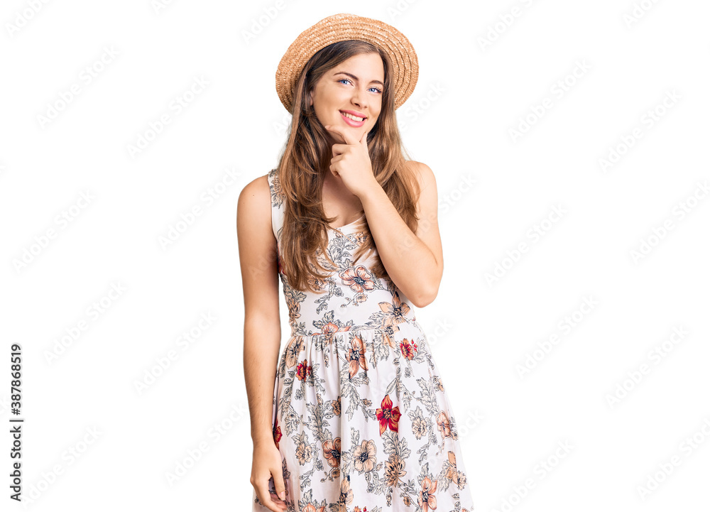 Beautiful caucasian young woman wearing summer hat looking confident at the camera smiling with crossed arms and hand raised on chin. thinking positive. Beautiful caucasian young woman wearing summer hat looking confident at the camera smiling with crossed arms and hand raised on chin. thinking positive.