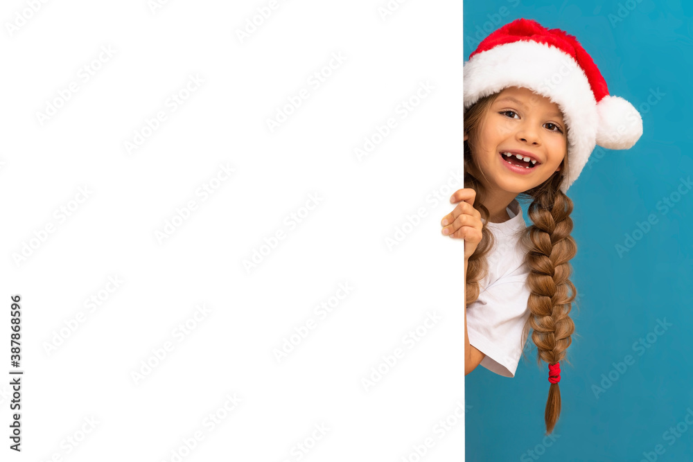 A little girl in a Christmas hat looks out from behind an ad. A little girl in a Christmas hat looks out from behind an ad.