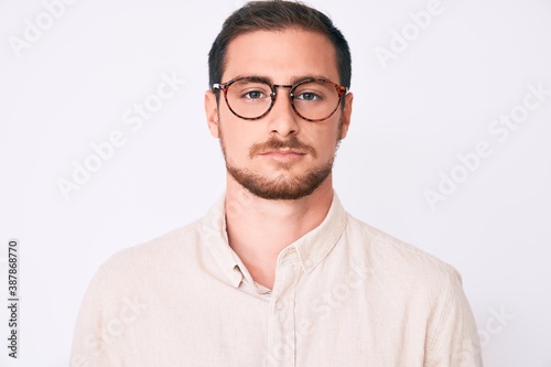 Young handsome man wearing casual clothes and glasses with serious expression on face. simple and natural looking at the camera.