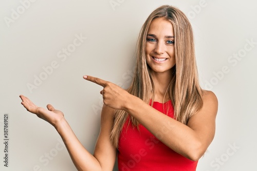 Young blonde woman wearing casual clothes amazed and smiling to the camera while presenting with hand and pointing with finger.