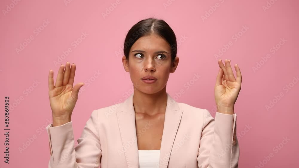 young businesswoman in pink suit rolling eyes, holding arms in the air and making a talking hands gesture on pink background