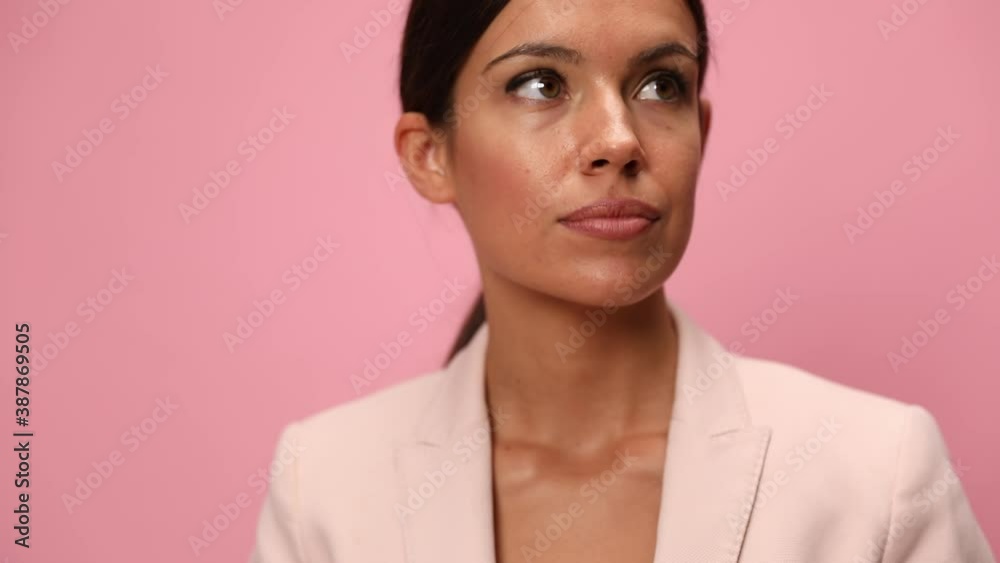 pensive young woman wearing pink suit looking to side, thinking and analyzing, holding hand to chin in an arrogant manner on pink background pensive young woman wearing pink suit looking to side, thinking and analyzing, holding hand to chin in an arrogant manner on pink background