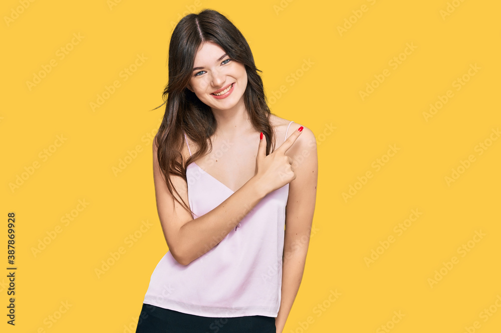Young beautiful caucasian girl wearing casual clothes cheerful with a smile of face pointing with hand and finger up to the side with happy and natural expression on face Young beautiful caucasian girl wearing casual clothes cheerful with a smile of face pointing with hand and finger up to the side with happy and natural expression on face