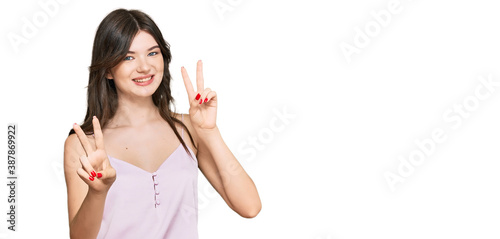 Young beautiful caucasian girl wearing casual clothes smiling looking to the camera showing fingers doing victory sign. number two.