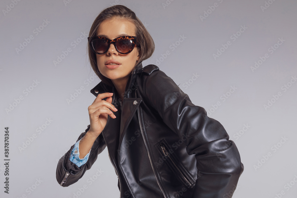 Young fashion model wearing leather jacket and sunglasses, standing Young fashion model wearing leather jacket and sunglasses, standing