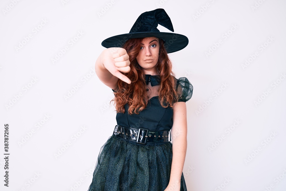 Young beautiful woman wearing witch halloween costume looking unhappy and angry showing rejection and negative with thumbs down gesture. bad expression. Young beautiful woman wearing witch halloween costume looking unhappy and angry showing rejection and negative with thumbs down gesture. bad expression.