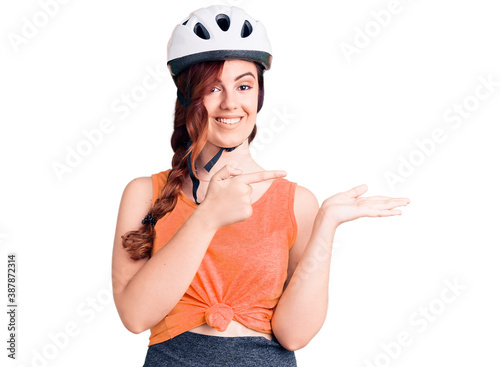 Young beautiful woman wearing bike helmet amazed and smiling to the camera while presenting with hand and pointing with finger.