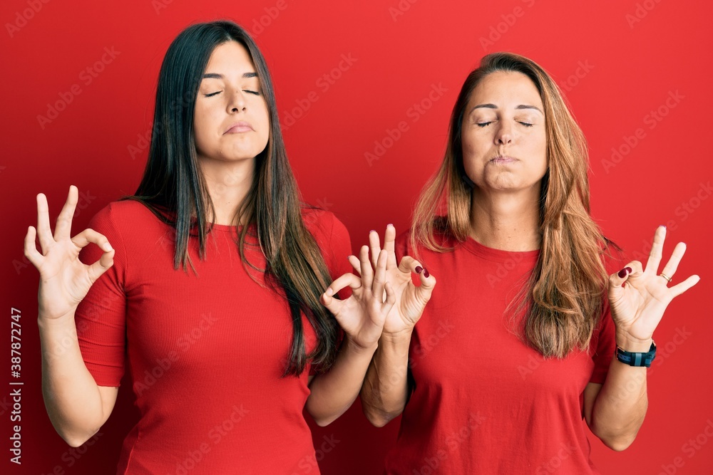 Hispanic family of mother and daughter wearing casual clothes over red background relaxed and smiling with eyes closed doing meditation gesture with fingers. yoga concept. Hispanic family of mother and daughter wearing casual clothes over red background relaxed and smiling with eyes closed doing meditation gesture with fingers. yoga concept.