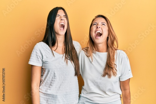 Hispanic family of mother and daughter wearing casual white tshirt angry and mad screaming frustrated and furious, shouting with anger. rage and aggressive concept.