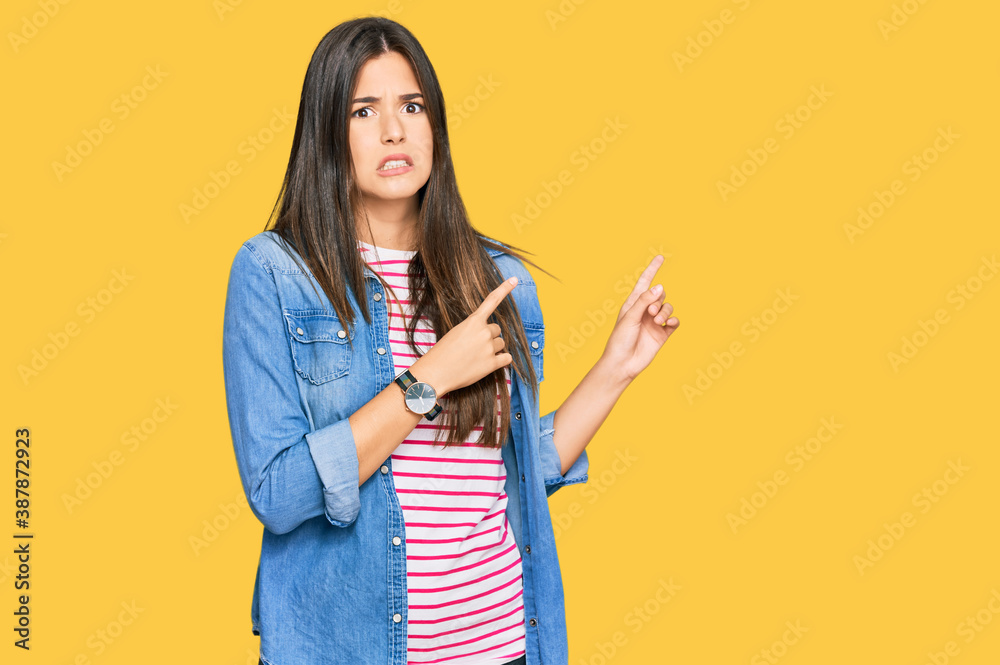 Young brunette woman wearing casual clothes pointing aside worried and nervous with both hands, concerned and surprised expression Young brunette woman wearing casual clothes pointing aside worried and nervous with both hands, concerned and surprised expression