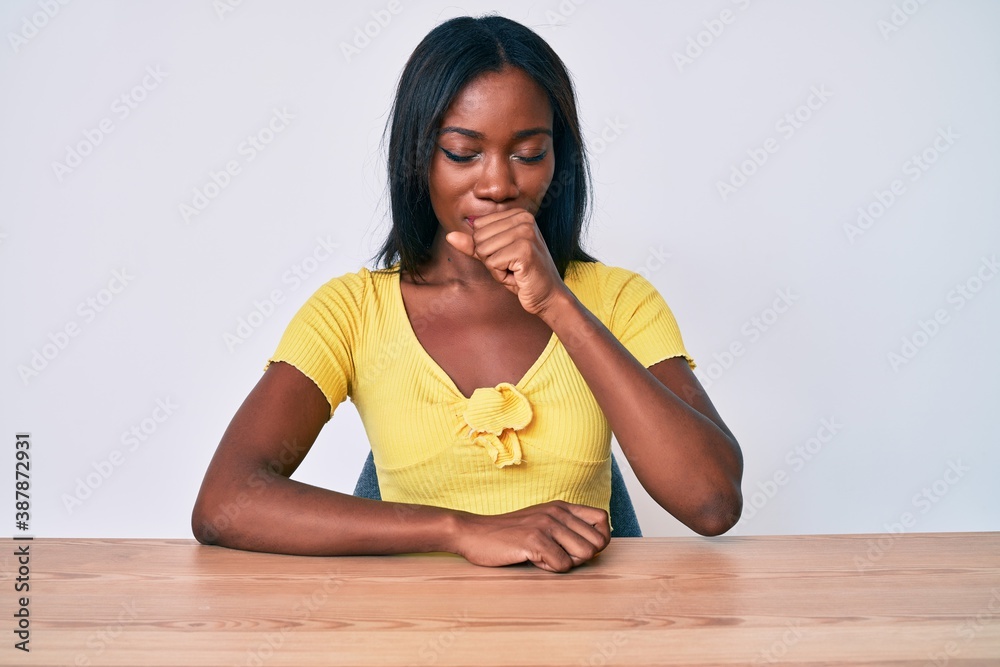 Young african american woman wearing casual clothes sitting on the table feeling unwell and coughing as symptom for cold or bronchitis. health care concept. Young african american woman wearing casual clothes sitting on the table feeling unwell and coughing as symptom for cold or bronchitis. health care concept.