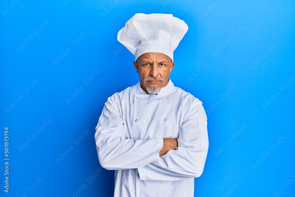 Middle age grey-haired man wearing professional cook uniform and hat skeptic and nervous, disapproving expression on face with crossed arms. negative person. Middle age grey-haired man wearing professional cook uniform and hat skeptic and nervous, disapproving expression on face with crossed arms. negative person.
