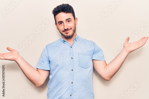 Young hispanic man wearing casual clothes clueless and confused with open arms, no idea and doubtful face.