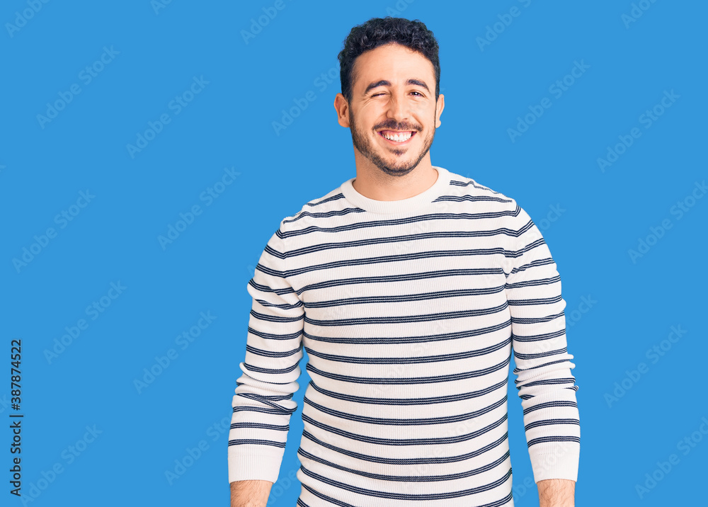 Young hispanic man wearing casual clothes winking looking at the camera with sexy expression, cheerful and happy face.
