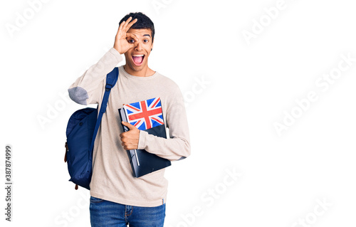 Young african amercian man wearing student backpack holding binder and uk flag smiling happy doing ok sign with hand on eye looking through fingers photo