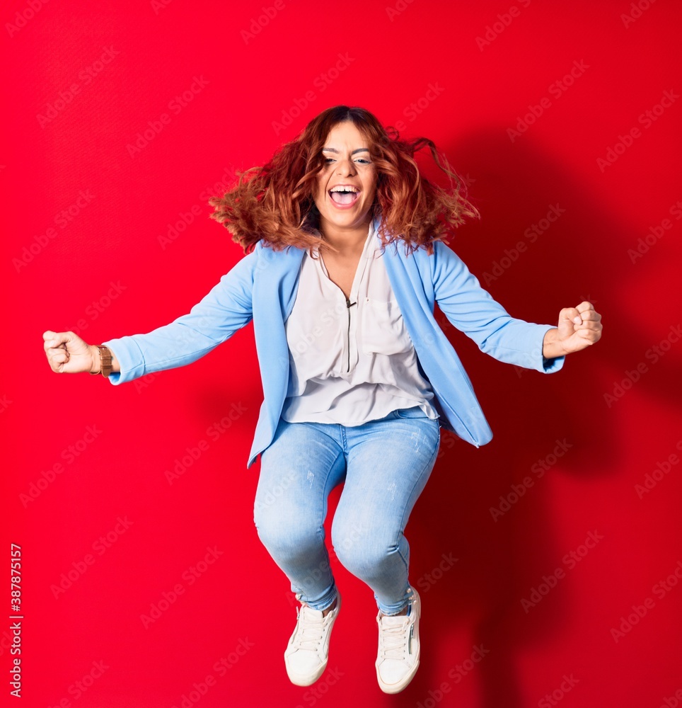 Young beautiful latin woman wearing casual clothes smiling happy. Jumping with smile on face doing winner gesture with fists up over isolated red background Young beautiful latin woman wearing casual clothes smiling happy. Jumping with smile on face doing winner gesture with fists up over isolated red background