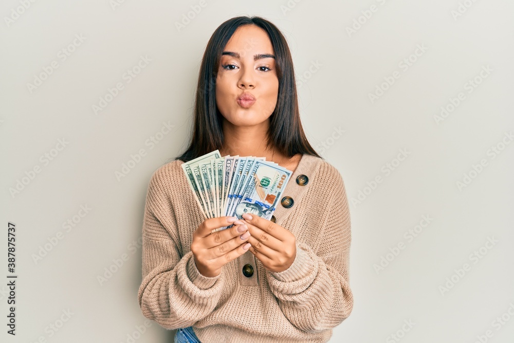 Young beautiful hispanic girl holding dollars looking at the camera blowing a kiss being lovely and sexy. love expression. Young beautiful hispanic girl holding dollars looking at the camera blowing a kiss being lovely and sexy. love expression.