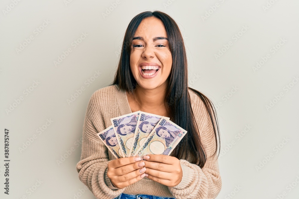 Young beautiful hispanic girl holding japanese yen banknotes smiling and laughing hard out loud because funny crazy joke. Young beautiful hispanic girl holding japanese yen banknotes smiling and laughing hard out loud because funny crazy joke.